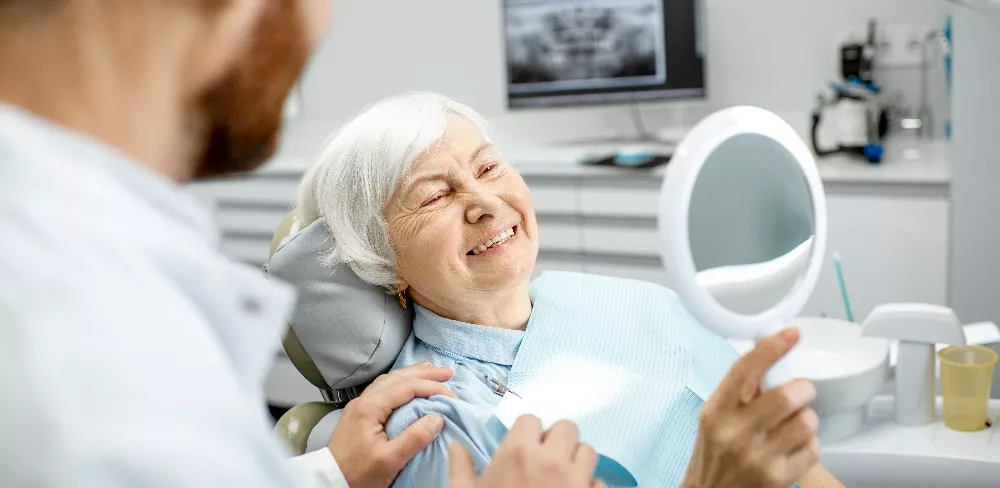 stock image of a woman in a oral surgeon's chair looking at her smile in a mirror. Used as the featured image on the dental implants page